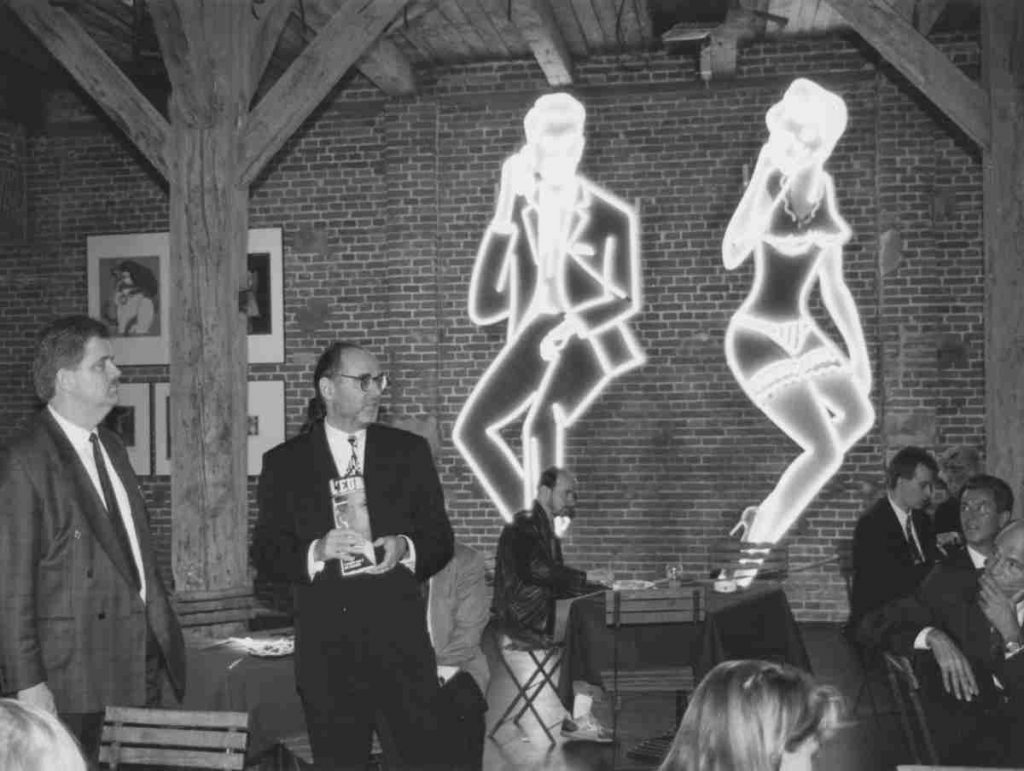 Claus Becker vor Neonreklamen mit Magazin in der Hand